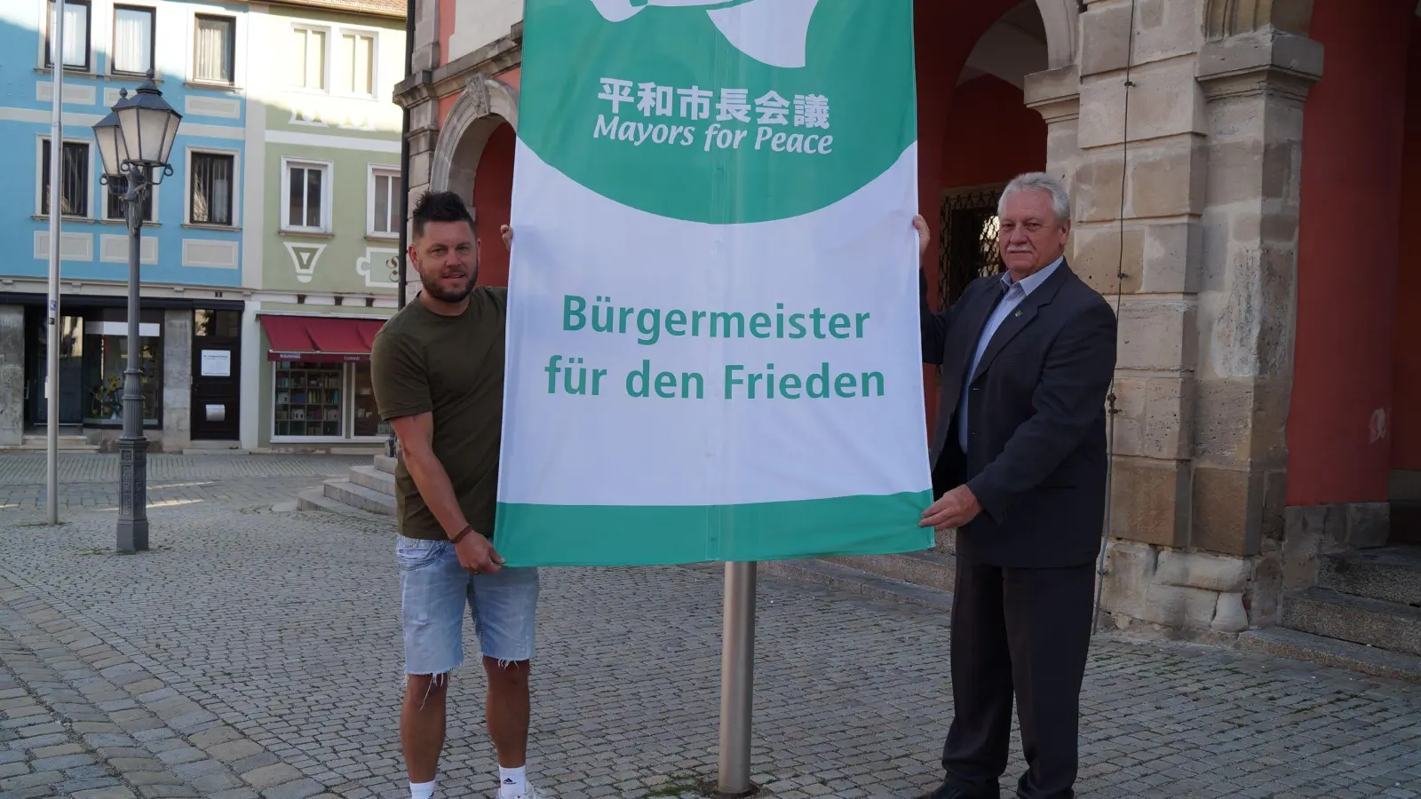 Mayors for Peace – Bürgermeister für den Frieden: Neustadts Stadtoberhaupt Klaus Meier (rechts) hisste gemeinsam mit dem städtischen Hausmeister Stephan Popp (links) die Friedensfahne am Marktplatz vor dem Rathaus. (Foto: Nicole Gunkel)