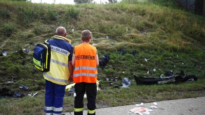 Ein Seelsorger und ein Mitglied der Feuerwehr an einer Unfallstelle auf der Autobahn 9 vor einer Böschung, die mit Trümmerteilen übersät ist. (Foto: Bodo Schackow/dpa)