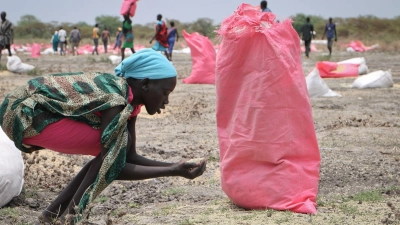 Eine Frau sammelt im südsudanesischen Kandak Hirse vom Boden auf, die in Säcken vom Welternährungsprogramm der Vereinten Nationen über der Stadt abgeworfen wurden. (Foto: Sam Mednick/AP/dpa)