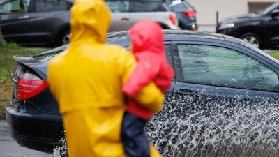 Eine Mutter und ihr Kind blicken auf eine teils überflutete Straße in Osnabrück. (Foto: Friso Gentsch/dpa)