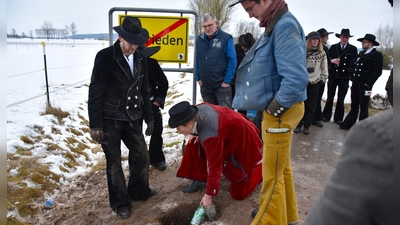 Begleiterin Fiona legte die Flaschen in das ausgebuddelte Loch, die Tim Oberfichtner (links) bei seiner Rückkehr nach mindestens drei Jahren wieder ausgraben und die halbe Flasche Schnaps als Dank für die erfolgreiche Walz mit Freunden austrinken wird. (Foto: Werner Wenk)