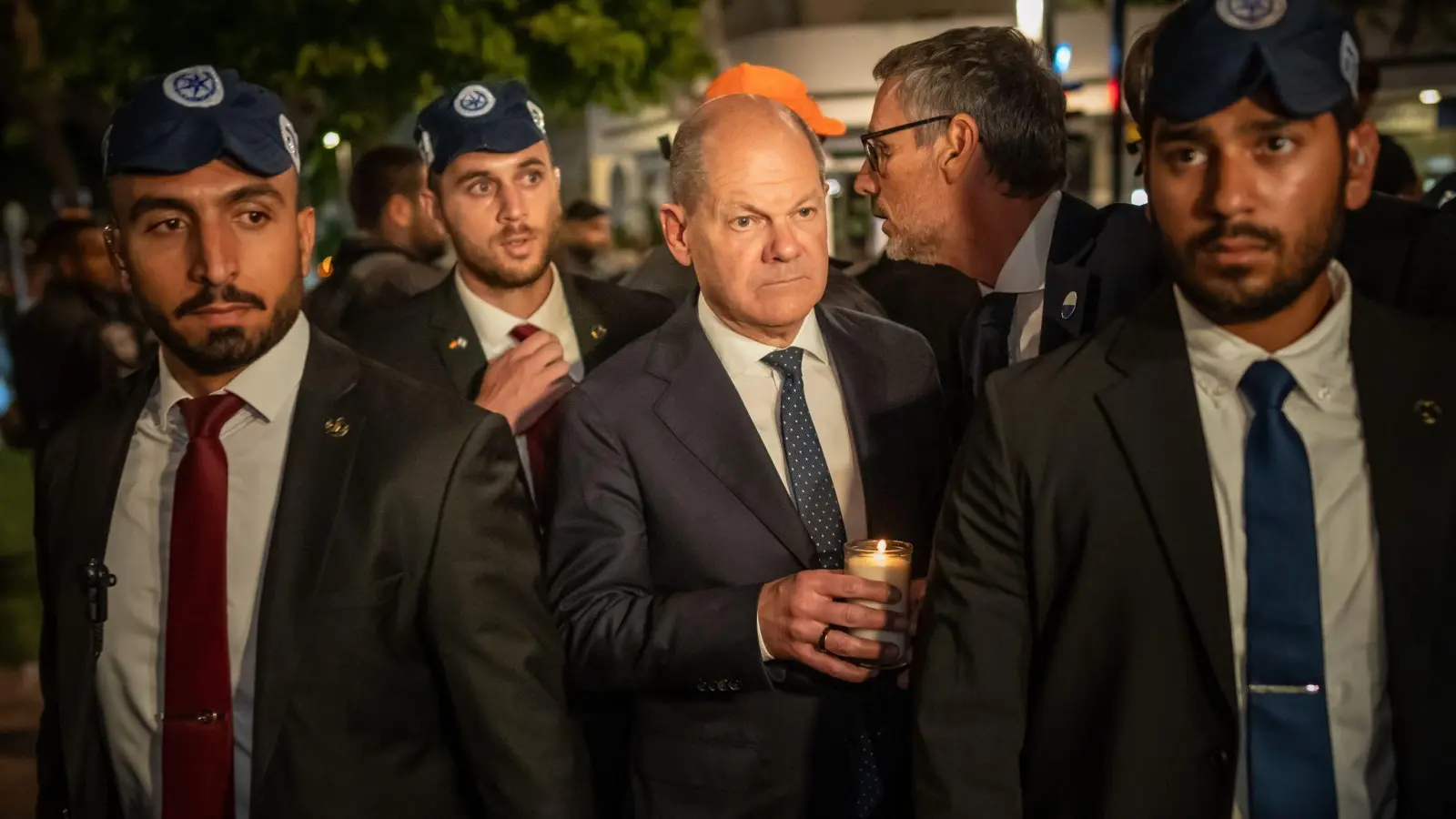 Bundeskanzler Olaf Scholz, umringt von Bodyguards, bei seinem Solidaritätsbesuch in Israel mit einer Kerze in der Hand am Dizengoff Square im Zentrum von Tel Aviv. (Foto: Michael Kappeler/dpa Pool/dpa)