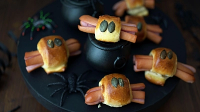 Für die Würstchenspinnen werden die an den Enden eingeschnittenen Wienerstückchen mit Teigstreifen umwickelt. Darauf drückt man je zwei Kürbiskerne als Augen und schiebt das Ganze in den Backofen. (Foto: Mareike Pucka/biskuitwerkstatt.de/dpa-tmn)