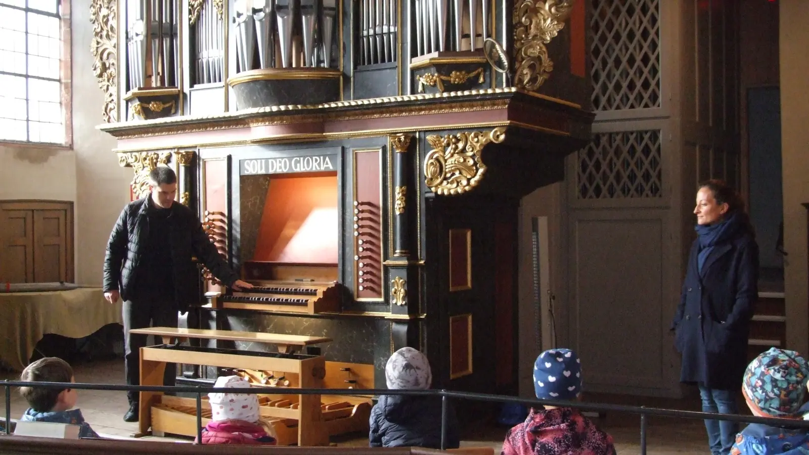 Die Mädchen und Jungen vom evangelischen Kindergarten Sandweg und Sopranistin Christiane Karg (rechts) hörten aufmerksam zu, als Dekanatskantor Micha Haupt (links) über die Orgel der Feuchtwanger Stiftskirche sprach. (Foto: Jasmin Kiendl)