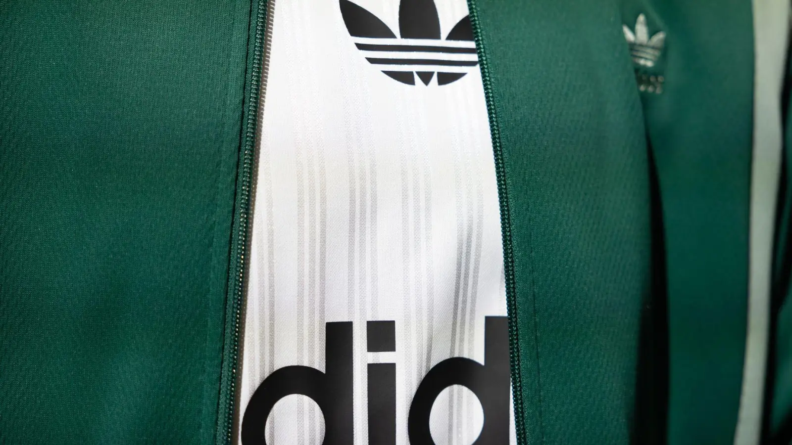 Das Logo und der Schriftzug von Adidas ist auf einem ausgestellten Kleidungsstück zu sehen. (Foto: Daniel Karmann/dpa/Symbolbild)