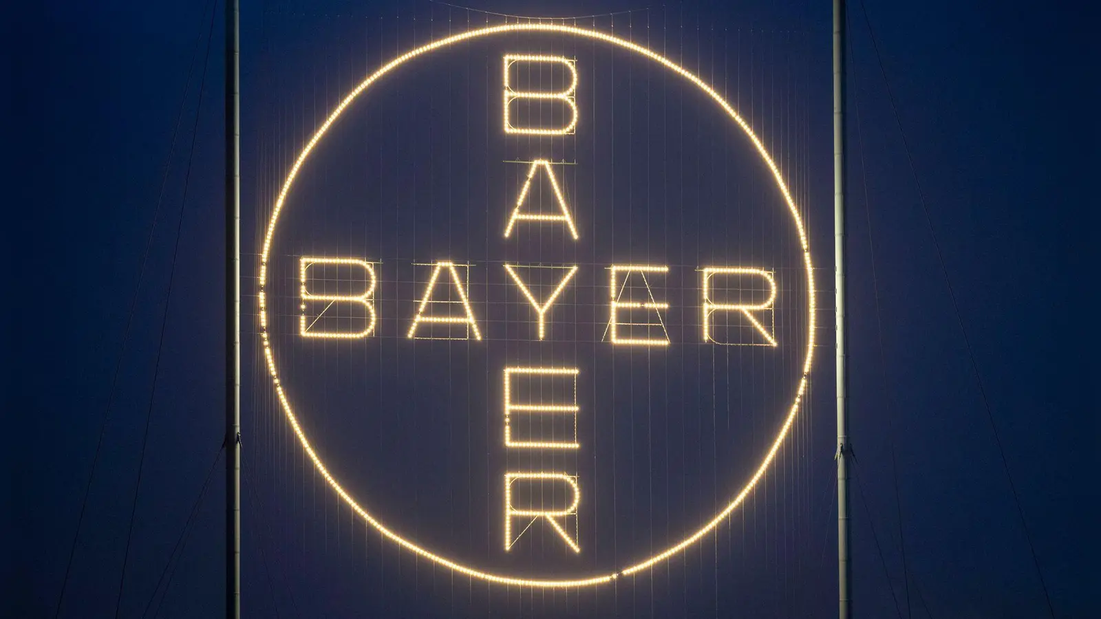 Das Bayer-Kreuz, das Logo des Unternehmens, leuchtet auf dem Werksgelände von Bayer in Leverkusen. (Foto: Thomas Banneyer/dpa)