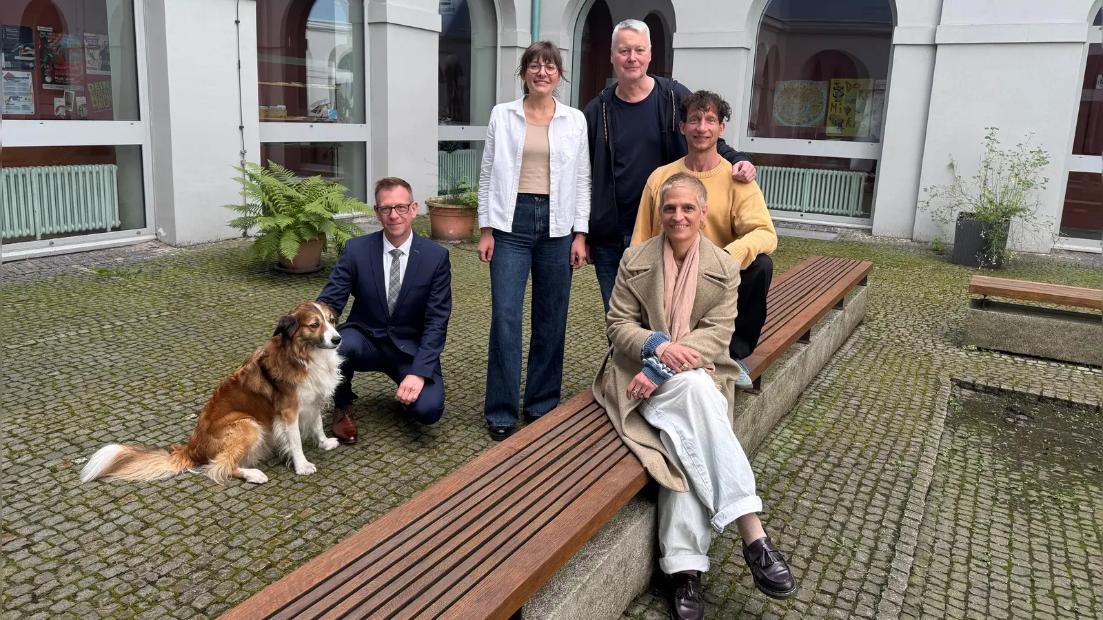 Im Innenhof des Gymnasium Carolinum, der zu den Spielorten des Wandeltheaterstücks gehört: Regisseurin Daniela Aue (vorne) sowie der Schauspieler Lukas Aue, der Komponist Stefan Kammerer, Chorleiterin Franziska Argmann und Schulleiter Stefan Exner (hinten von rechts). Daniela Aues Hund Elmo ist bei den Proben dabei.  (Foto: Lara Hausleitner)