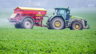 Ein Traktor fährt mit einem Streuwagen über ein Feld und bringt Dünger aus. (Foto: dpa)