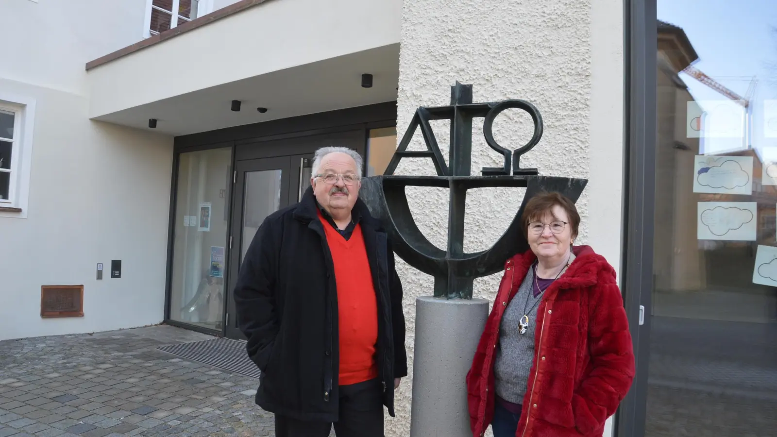 Hermann und Renate Rummel vor dem Haus der Kirche. Die Stele zeigt Alpha und Omega, für Hermann Rummel ein Lebensmotto, denn Jesus Christus umschließt die Welt, seine Kirche und unser Leben. (Foto: Peter Tippl)