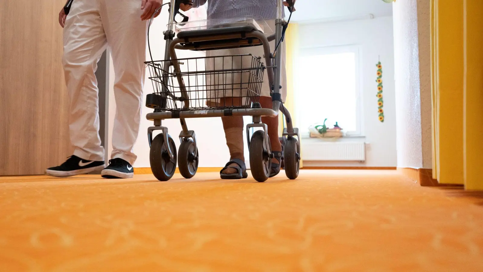 Ein Betreuer geht in einem Pflegeheim mit einer Bewohnerin über den Flur. (Foto: Bernd Weißbrod/dpa/Symbolbild)