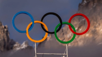 Die Olympischen Ringe auf dem Dach der Curling Halle sind vor den Bergen in Cortina zu sehen. Die Olympischen Winterspiele 2026 finden in Mailand und Cortina d'Ampezzo statt. (Foto: Michael Kappeler/dpa)