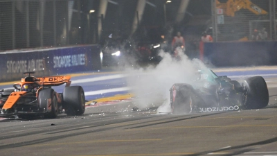 Nach einem Unfall steigt aus dem Auto von Lance Stroll (r) Rauch auf, während Oscar Piastri an der Unfallstelle vorbeifährt. (Foto: Caroline Chia/Reuters Pool/AP/dpa)