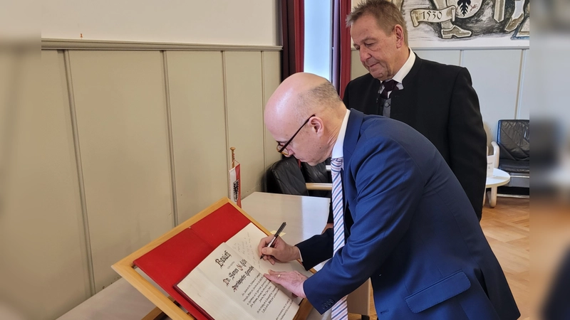 Der Generalkonsul Dr. James Miller (vorne) hat sich unter den Augen von drittem Bürgermeister Roland Reichenberg (hinten) ins Goldene Buch der Stadt Bad Windsheim eingetragen. (Foto: Nina Daebel)
