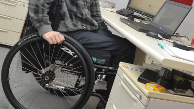 Ein Mann sitzt in einem Rollstuhl an seinem Arbeitsplatz am Schreibtisch. (Foto: Stefan Puchner/dpa)