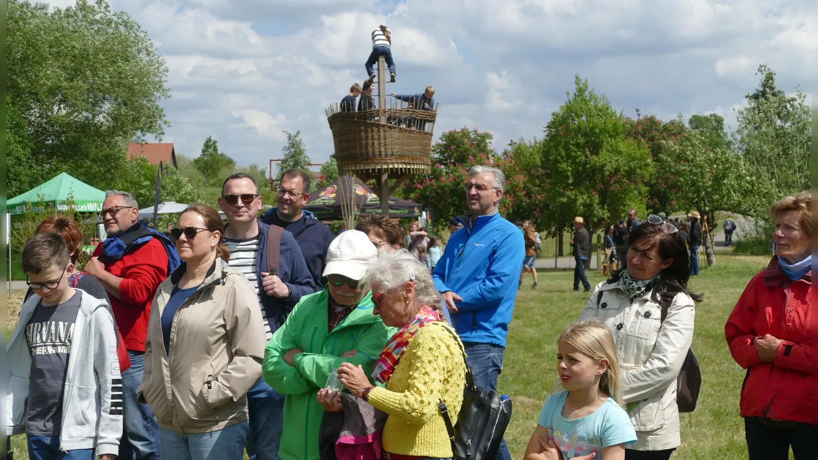 Die Teilnehmer eines Rundgangs durch die Streuobstwiesen schauen sich Kokons der Seidenraupe an. Im Hintergrund ist das Krähennest zu erkennen, ein Spielturm, der bei Kindern sehr beliebt ist. (Foto: Helmut Meixner)