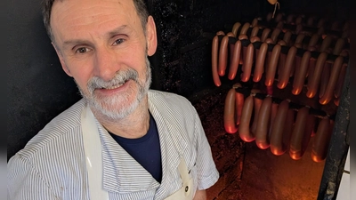 Metzgermeister Friedrich Menhorn kontrolliert das Buchenholzfeuer, über dem die Würste geräuchert werden. (Foto: Friedrich Zinnecker)