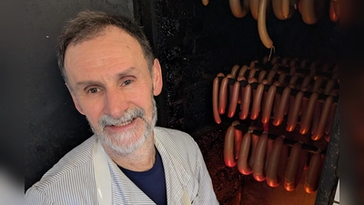 Metzgermeister Friedrich Menhorn kontrolliert das Buchenholzfeuer, über dem die Würste geräuchert werden. (Foto: Friedrich Zinnecker)