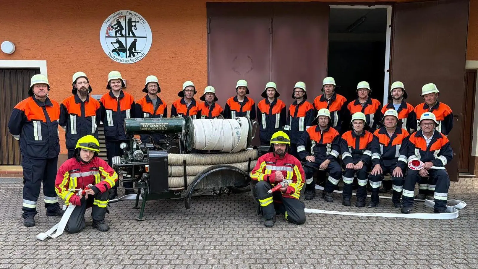 Auf 25 Aktive bringt es die Feuerwehr Tauberscheckenbach derzeit. Ein paar davon fehlen auf dem Foto mit der alten Spritze aus dem letzten Jahrhundert als Blickfang. Kommandant Denny Döppert ist sitzend als Vierter von rechts zu sehen, vorne die Atemschutzräger Leander Bach (links) und Uwe Stahl. (Foto: Freiwillige Feuerwehr Tauberscheckenbach)