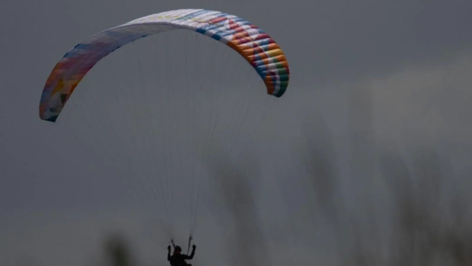 Ein Gleitschirmflieger wird von der Sonne angeschienen während er in einer Wiese landet. (Foto: Sebastian Gollnow/dpa)