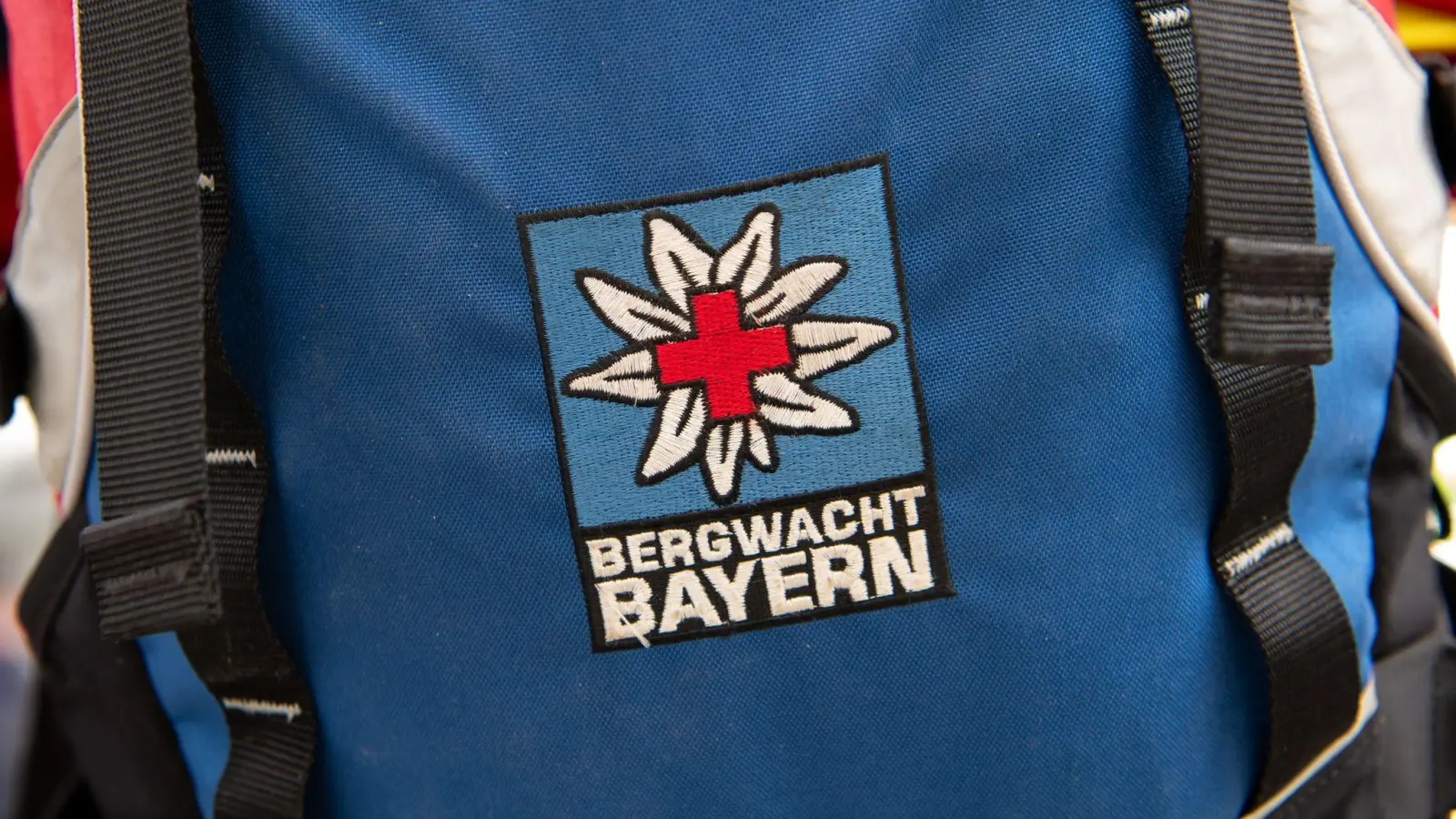 Das Logo der Bergwacht ist an einem Rucksack zu sehen. Bei Oberstdorf musste die Bergwacht nun einen Mann retten, der ohne richtige Ausrüstung und Erfahrung zwei Nächte in den Bergen verbrachte. (Archivfoto-Illustration) (Foto: Sven Hoppe/dpa)