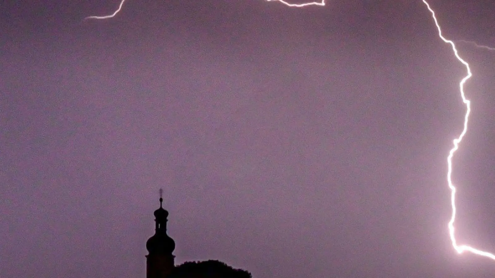 Blitze entladen sich aus einer Gewitterwolke über einer Kirche in Niederbayern. (Foto: Armin Weigel/dpa/Archivbild)