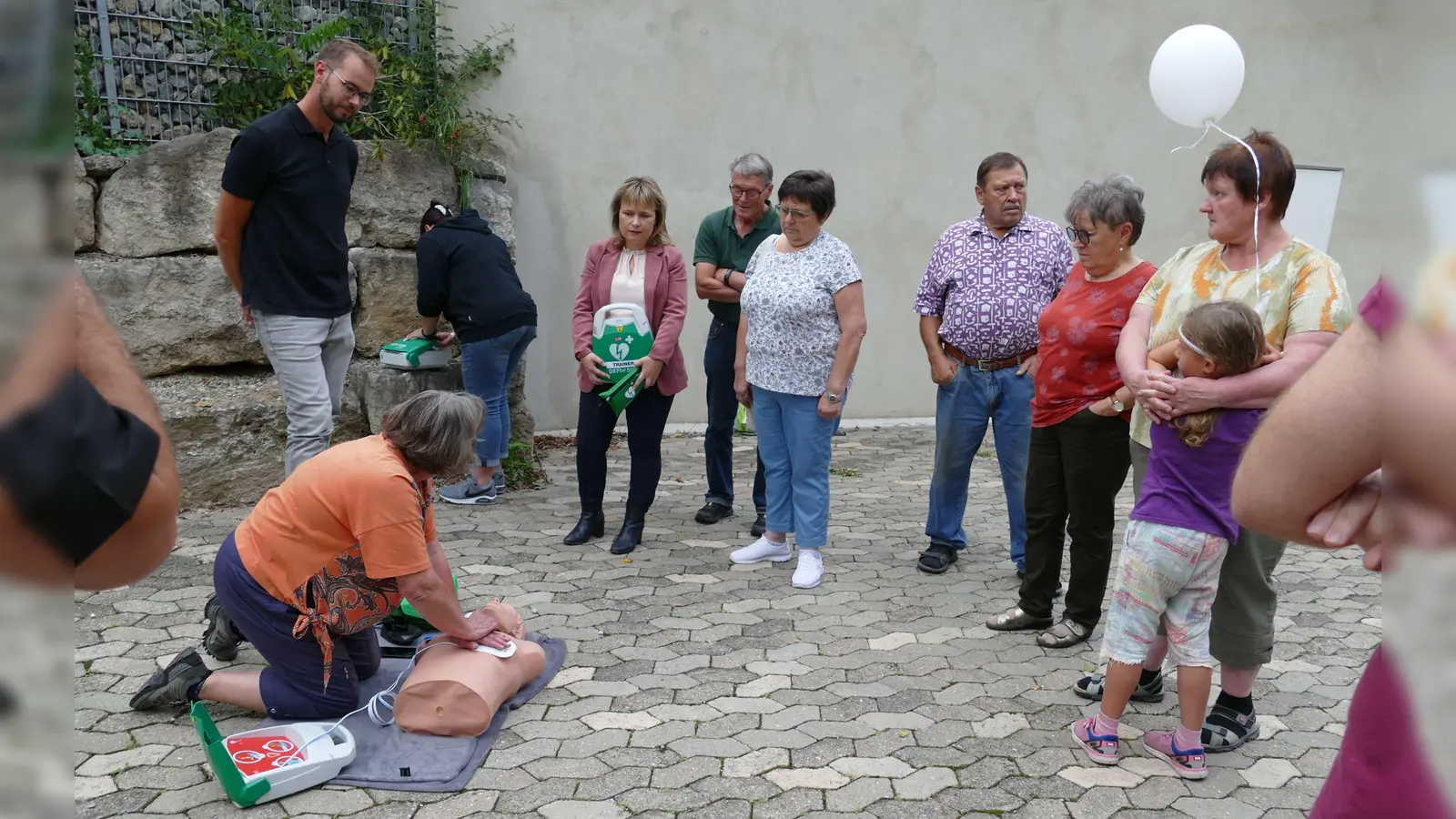 „Das ist ja ganz schön anstrengend so eine Herzdruckmassage“ , stellte eine Adelsdorferin (kniend) fest, die unter Anleitung von Ludwig Winter (links), Silvia Heubeck (Mitte) und Claudia Wust (Dritte von links) versuchte, den Patienten – in diesem Fall eine lebensgroße Puppe – mit Hilfe eines Defibrillators am Leben zu erhalten. (Foto: Sylvia Fehlinger)