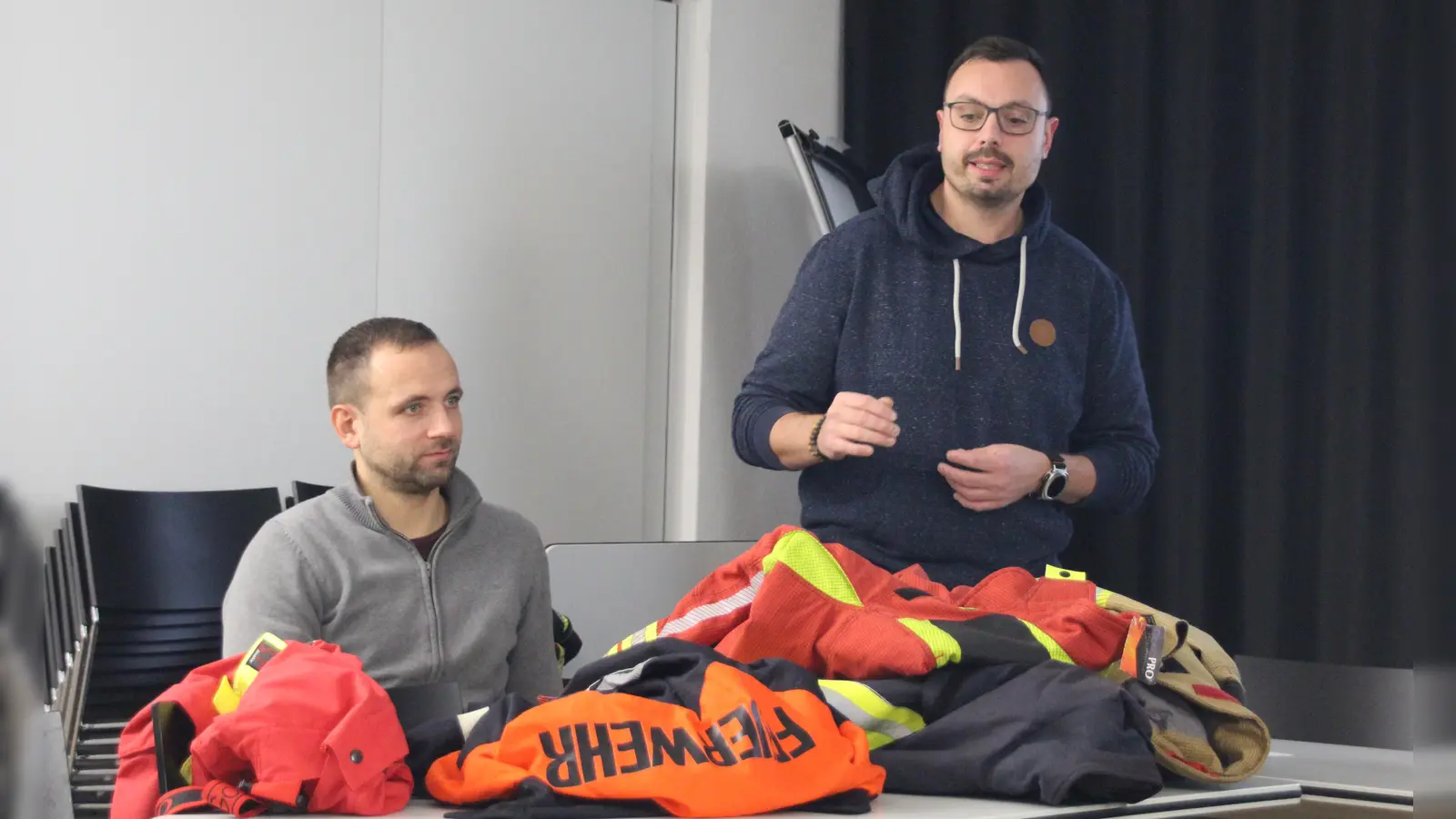 Feuerwehrkommandant Patrick Noll (stehend) hatte verschiedene Modelle mitgebracht, damit die Stadträte ein Bild davon haben, was die Unterschiede der Feuerwehrjacken und -hosen sind. Kämmerer Heiko Wittig ist in der Verwaltung für das Feuerwehrwesen zuständig. (Foto: Robert Maurer)