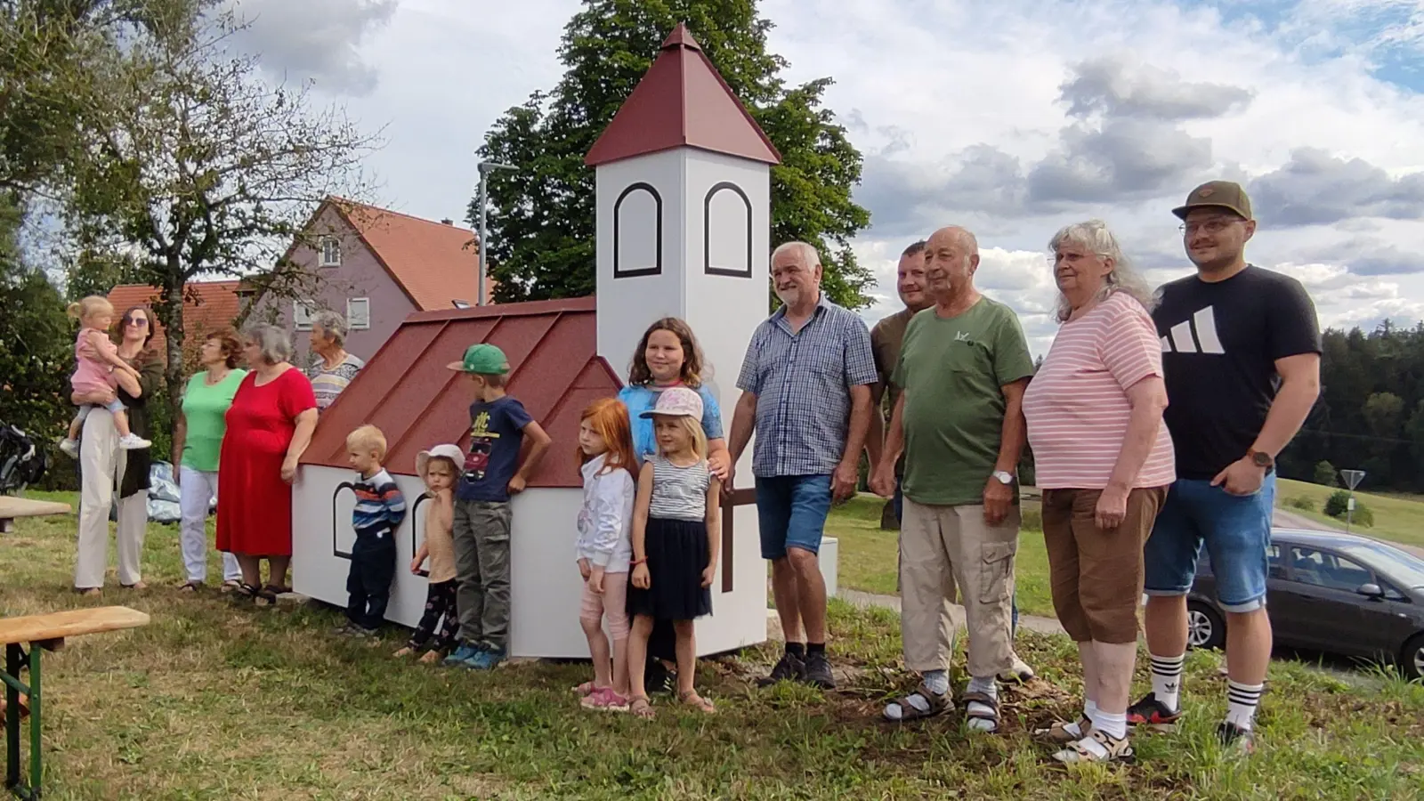 Am künftigen Standort der Kapelle in Aichau steht jetzt deren Modell im Maßstab 1:4. Bis zum Baubeginn dient es als Werbung für das Projekt, das ein eigens gegründeter Verein trägt. Diesem gehören Mitglieder aus vier Generationen an, Vorsitzender ist Emil Geißler (Fünfter von rechts). (Foto: Kapelle Aichau e.V./Edith Geißler)