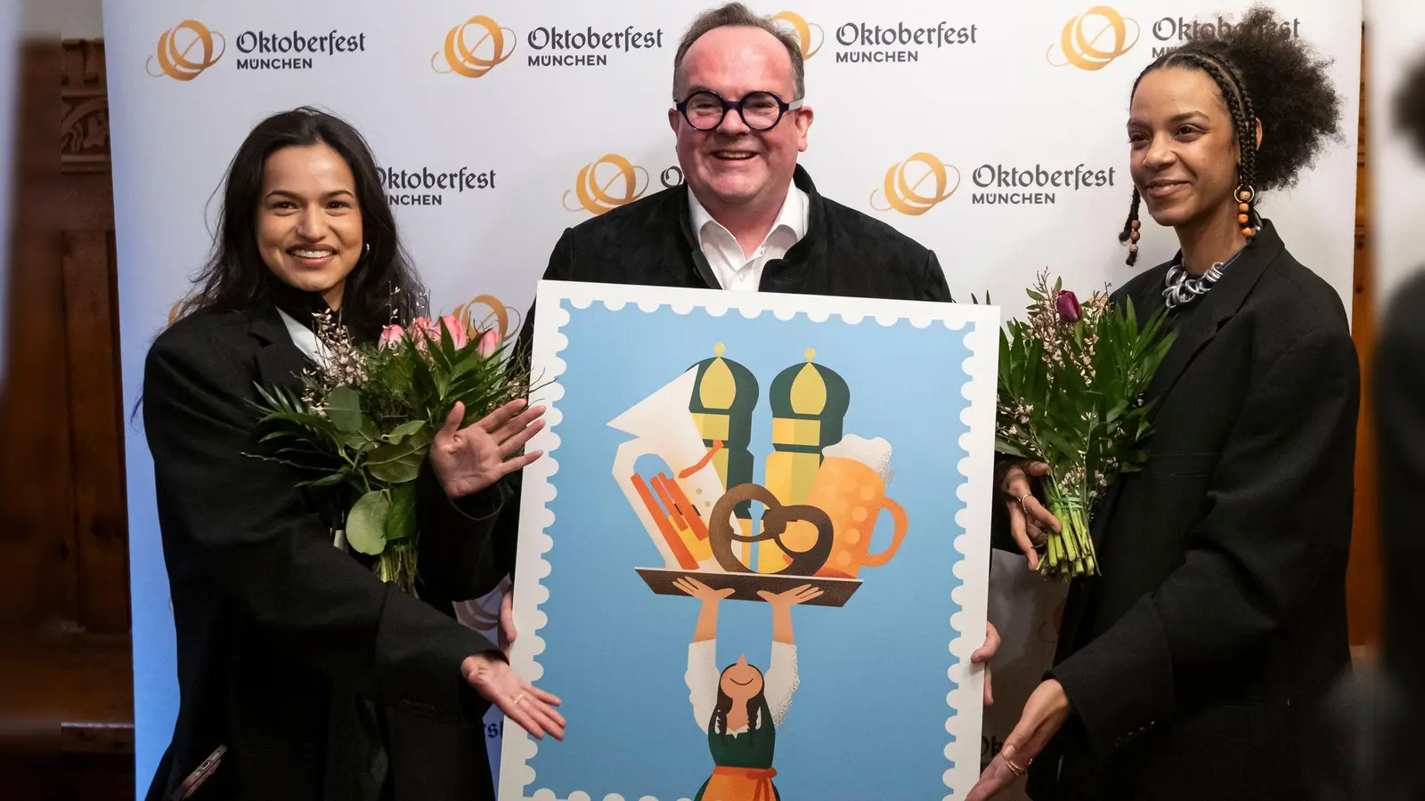 Wiesnchef Clemens Baumgärtner (M.) präsentiert mit den Künstlerinnen Amiera Harithas (l.) und Dinah-Charles Francis das offizielle Motiv zum Oktoberfest 2025. (Foto: Lukas Barth/dpa)