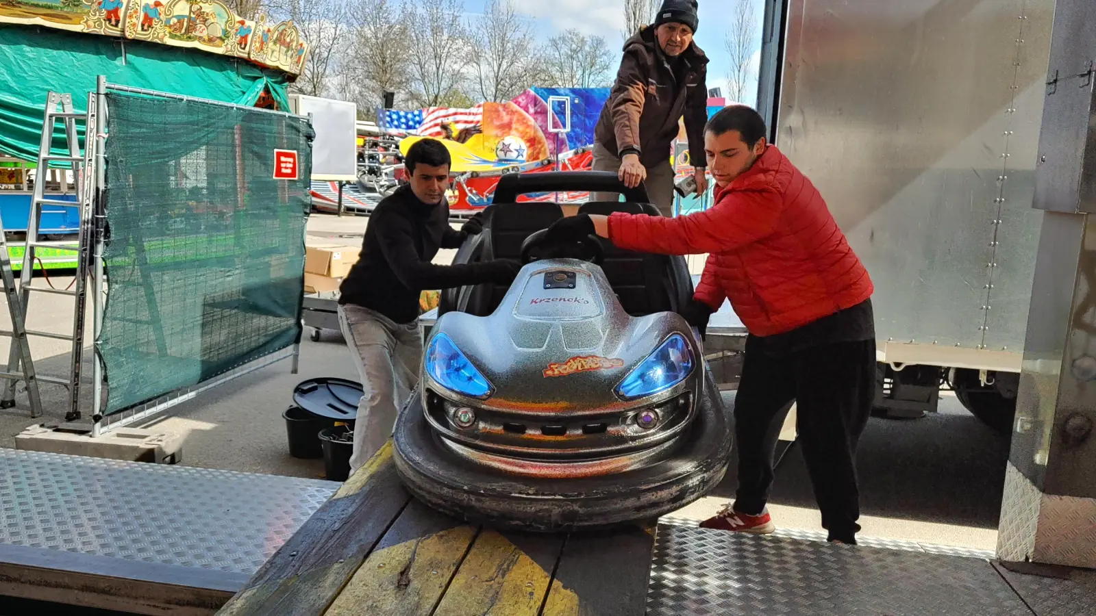 Einige Fahrgeschäfte für das Frühlingsfest stehen schon. Denis Krzenck (hinten) und sein Team rollen die ersten Autos auf die Plattform des Autoscooters. (Foto: Katrin Merklein)