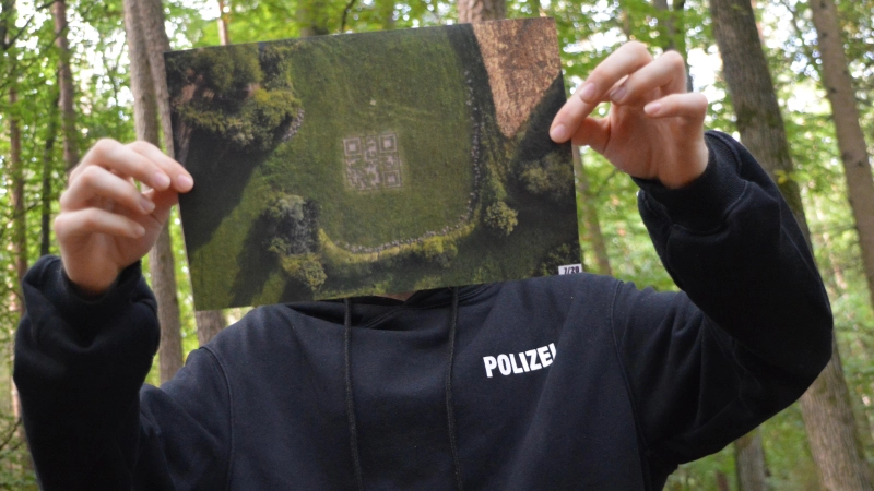 Damit „Ra.g.e.“ unerkannt bleibt, hält er sich ein Drohnenfoto seines QR-Codes vors Gesicht. (Foto: Johannes Zimmermann)