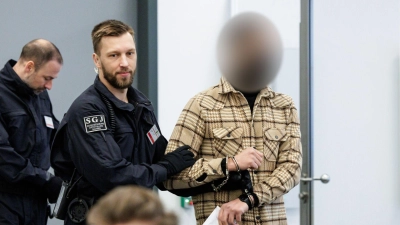 Ein Angeklagter (r) wird von Justizbeamten in Handschellen in den Gerichtssaal des Oberlandesgerichts Dresden geführt. (Foto: Jens Schlueter/POOL AFP/dpa)