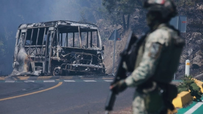 Ein Soldat steht in Mexiko - einem der drei Ausrichterländer der Fußball-WM im Sommer - neben einem ausgebrannten Bus. (Foto: Armando Solis/AP/dpa)