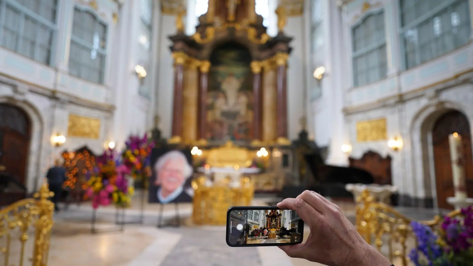 Ein Besucher macht zu Beginn der Trauerfeier ein Foto mit einem Smartphone. (Foto: Marcus Brandt/dpa)