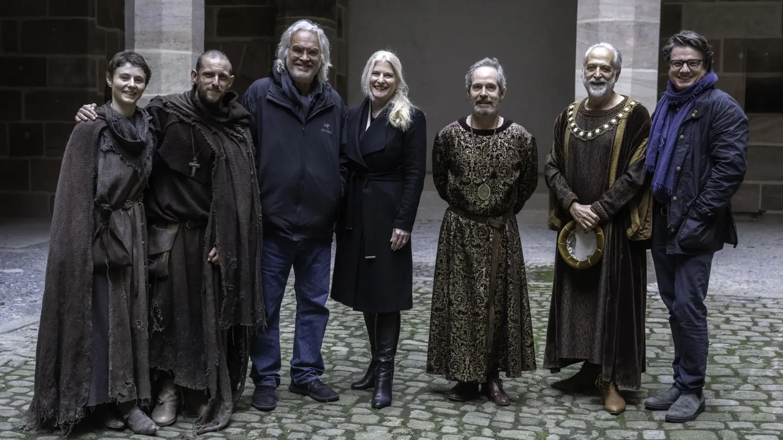 Mitglieder des Casts von „The Uprising” zeigen sich im Innenhof des Pellerhauses in Nürnberg im Kostüm (v.l.): Thomasin McKenzie, Jamie Bell, Regisseur Paul Greengrass, Judith Erber (FFF Bayern), Tom Hollander, Mark Redhead sowie Philipp Kreuzer (Produzent, Supernix). (Foto: Betina la Plante/FFF Bayern)