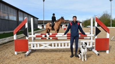 Den ehemaligen Dressurplatz hat der neue Pächter Julius Ehinger bereits zum Springplatz umfunktioniert. Immer mit dabei: Hündin Lotte. Im Hintergrund posiert Reiterin Lisa Engel auf „Le Vagabond“. (Foto: Anita Dlugoß)