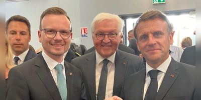 Bezirkstagspräsident Peter Daniel Forster sprach in Oradour mit Bundespräsident Frank-Walter Steinmeier und Staatspräsident Emmanuel Macron (von links). Er hatte für sie einen Europa-Wein aus Ipsheim und ein Buch über die kommunalen Freundschaften mitgebracht. (Foto: Bezirk Mittelfranken/Wolf Dieter Enser)