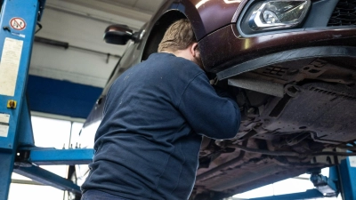 Ein Mechaniker schaut in einer Kfz-Werkstatt in den Radkasten eines Autos. (Foto: Hannes P. Albert/dpa)