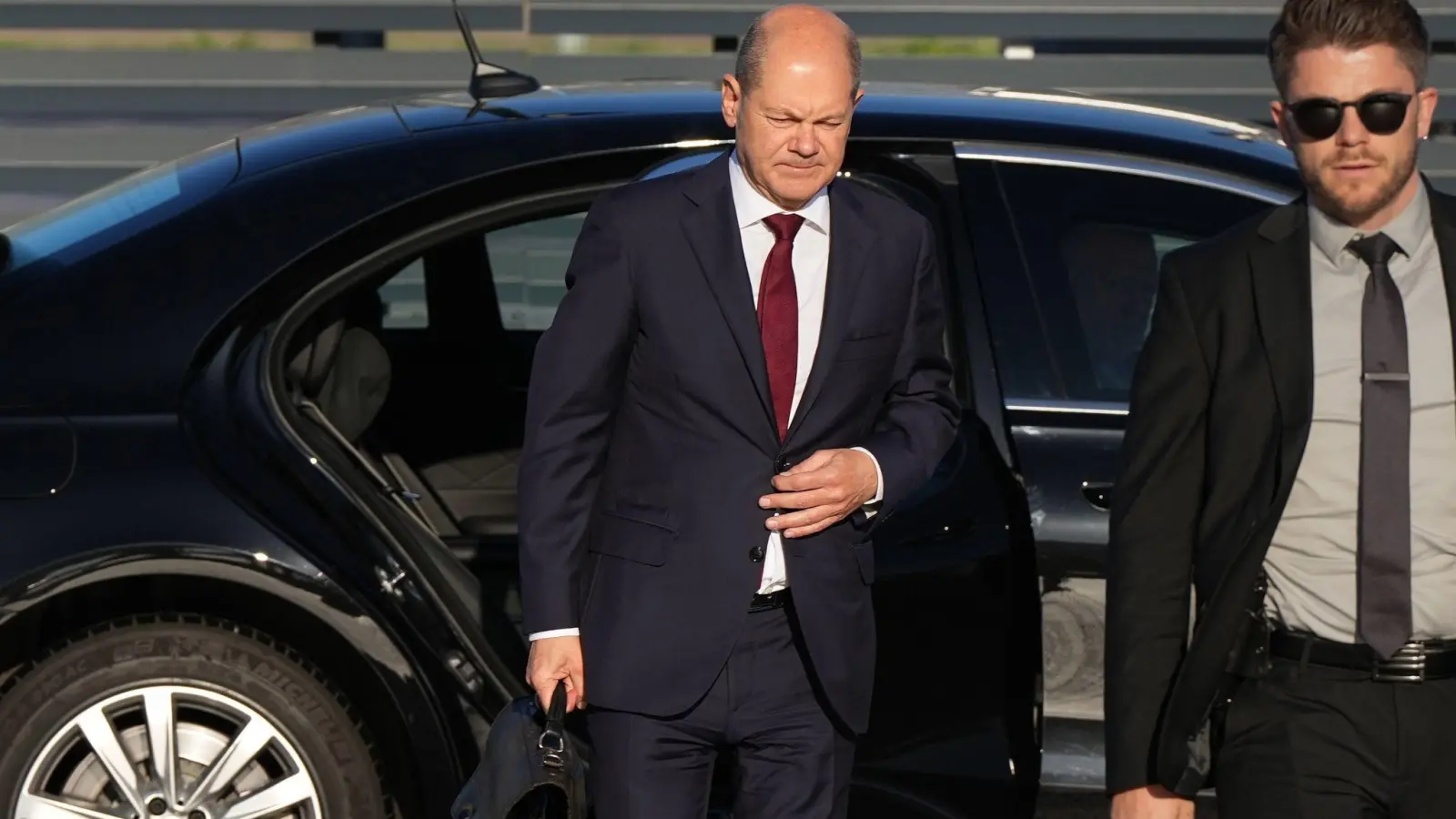 Bundeskanzler Olaf Scholz (l, SPD) kommt zum Start einer zweitägigen Reise auf dem militärischen Teil des Flughafens Berlin Brandenburg BER an und steigt aus einer Limousine. (Foto: Soeren Stache/dpa)