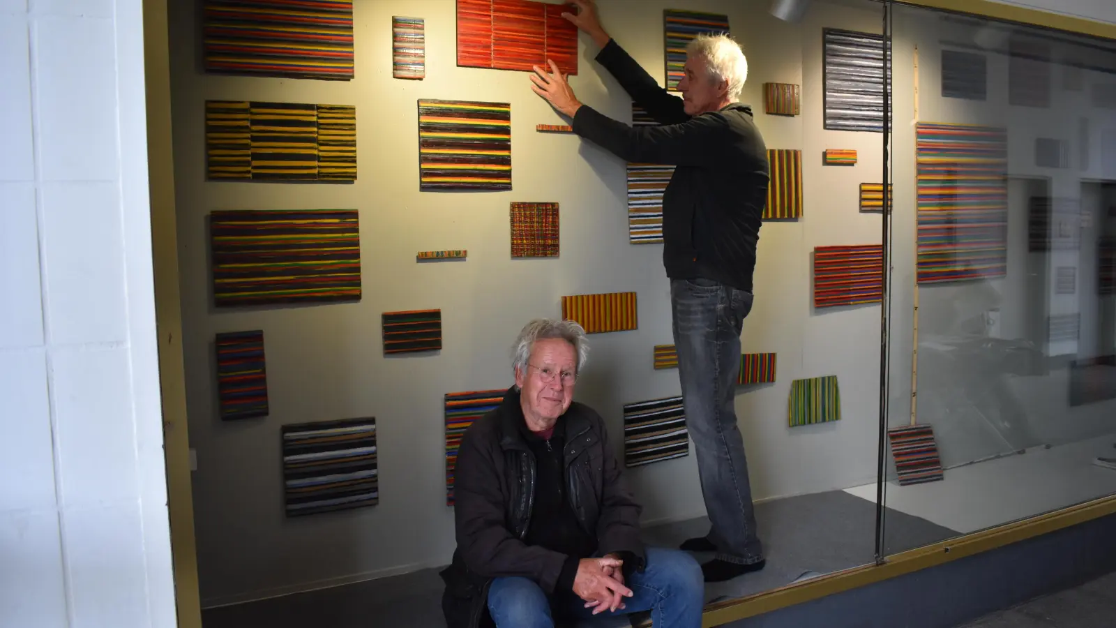 Dietmar Lisson (rechts) half Hasso von Henninges beim Aufhängen seiner Exponate. Zu sehen sind rund 50 seiner Arbeiten mit dem Titel „Farbenfroh” im Schaufenster des Neustädter Bahnhofsgebäudes. (Foto: Ute Niephaus)
