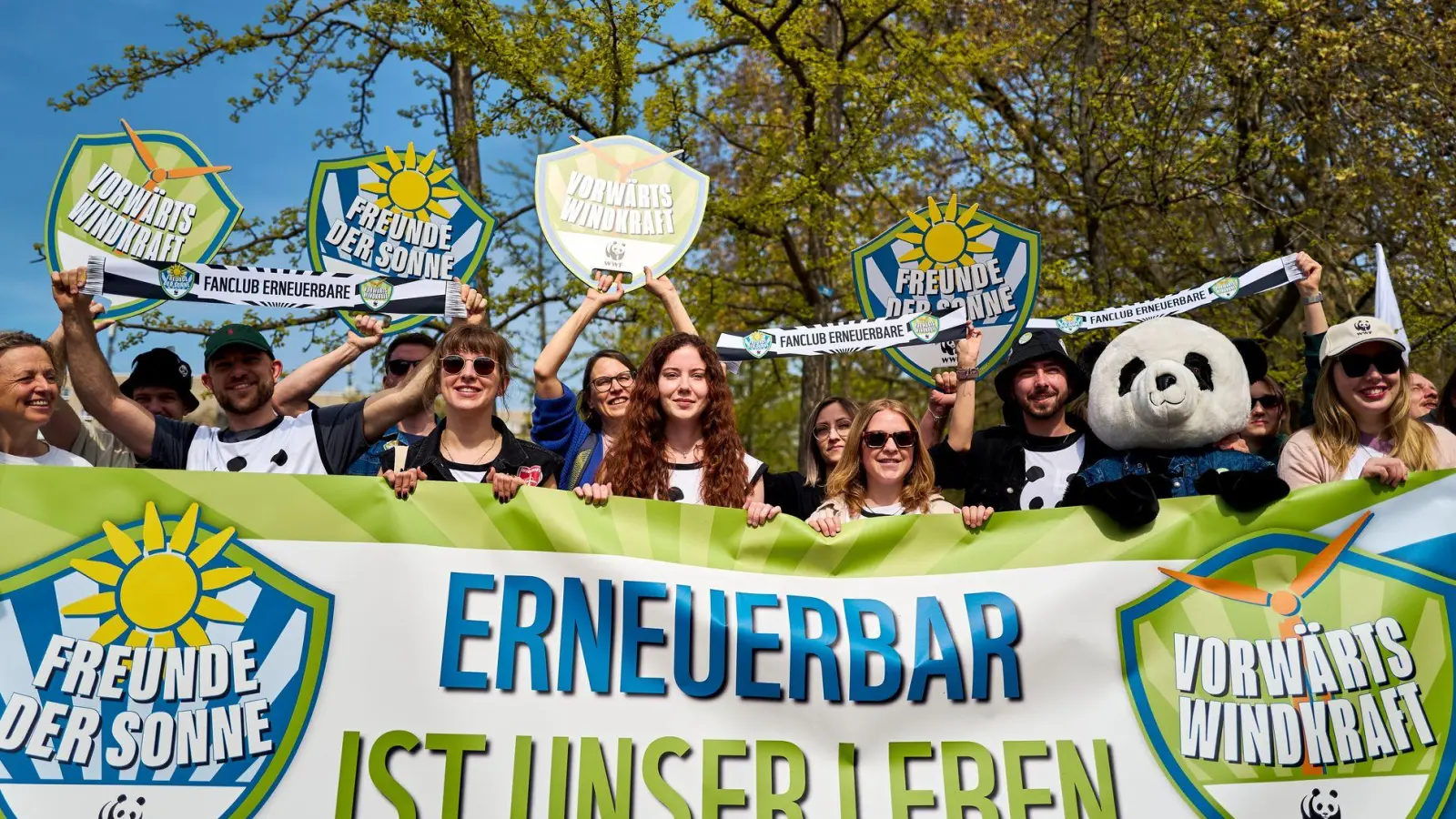Demonstrierende halten ein Banner und Schilder in die Höhe, darunter eine Person im Pandakostüm. (Foto: Michael Ukas/dpa)
