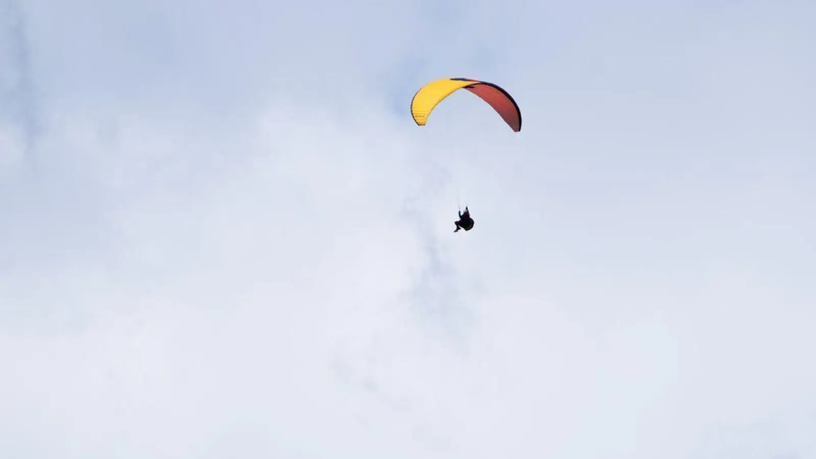 Ein Paraglider fliegt bei teilweise blauem Himmel an einem Berg vorbei. (Foto: Nicolas Armer/dpa)