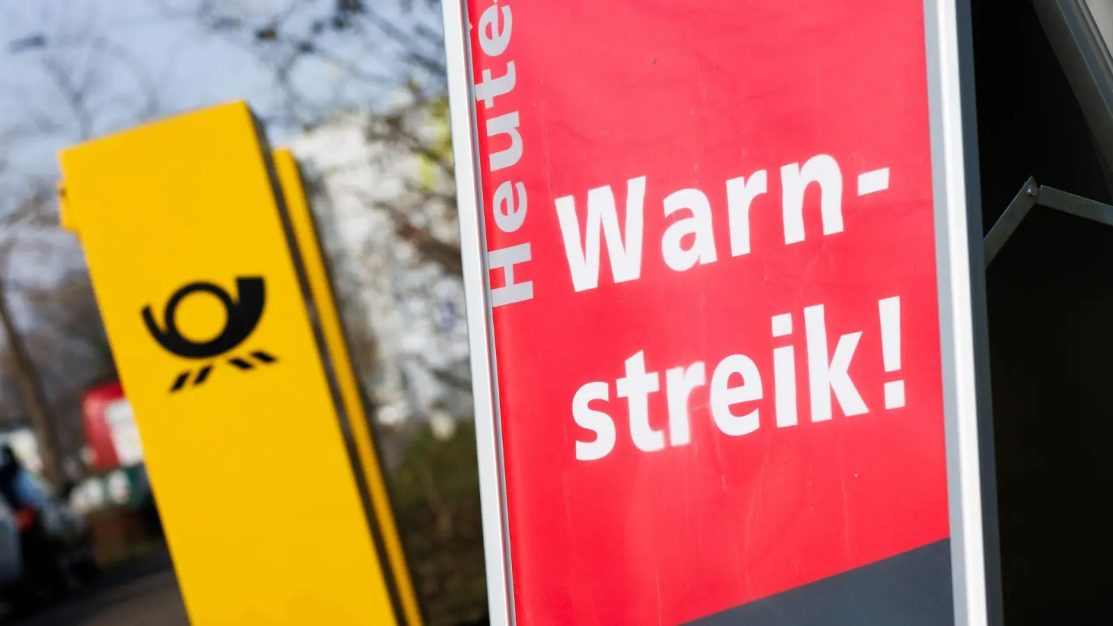 Ein Warnstreik-Schild bei einem Post-Standort, daneben ein Briefkasten - im Ringen um einen Tarifabschluss haben Tausende Postler erneut die Arbeit niedergelegt. (Foto: Philipp von Ditfurth/dpa)