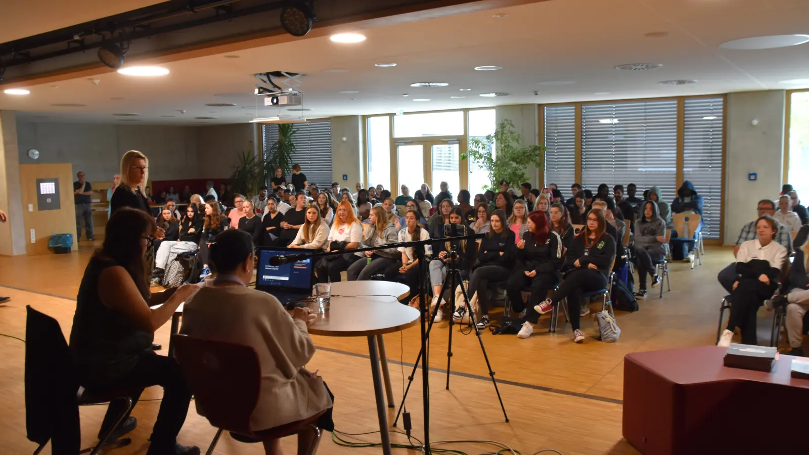 BSZ-Leiterin Bettina Scheckel (stehend) und die beiden Gastrednerinnen Birgit Mair (sitzend, links) und Eva Franz sprachen von der Bühne der Gymnasiumsaula. (Foto: Andreas Reum)