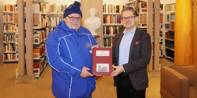 Fritz Heubeck (links) übergibt Bibliotheksleiter Christian Mantsch ein Exemplar seines „Chronologischen Geschichtsbuchs des Ansbacher Weihnachtsmarktes”. (Foto: Oliver Herbst)