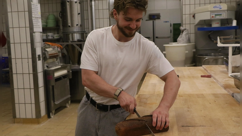 Maximilian Wimmer halbiert in seiner Bäckerei das Brot mit dem Messer und wiegt nicht nach. (Foto: Alexander Rausch)