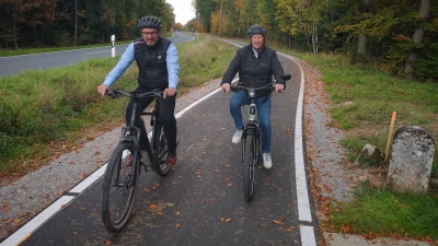 Auf halbem Weg zwischen Dombühl und Schillingsfürst trafen sich die beiden Bürgermeister Jürgen Geier (links) und Michael Trzybinski am Mittwoch mit ihren E-Bikes für eine kurze Einweihungsfahrt. Rechts steht der Grenzstein, der den Übergang der beiden Gemeindegebiete markiert. (Foto: Jürgen Binder)