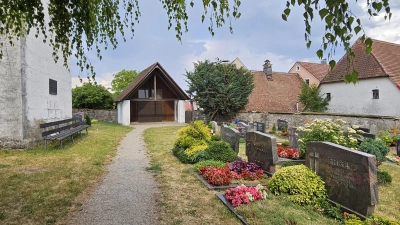 In die Jahre gekommen ist die Leichenhalle (Mitte) am Friedhof in Neunkirchen, im Schatten der Kirche St. Georg (links). Wer für den Unterhalt aufkommen muss, ist unklar. (Foto: Wolfgang Grebenhof)