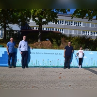 Mehrere Betonwände sind nun künstlerisch gestaltet. Das Bild zeigt (von links) Hausmeister Michael Lorenz, Bürgermeister Thomas Schmitt, Künstler Azar Valizada und Schülerin Laila Abd el Salam. (Foto: Gerhard Krämer)