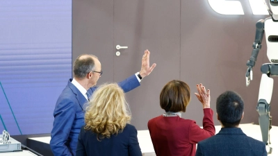 Bundeskanzler Friedrich Merz winkt einem Roboter zu – die Zukunft winkt zurück. (Foto: Michael Matthey/dpa)
